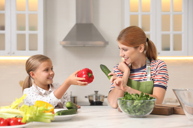 Photo of Mother and daughter cooking salad together in kitchen