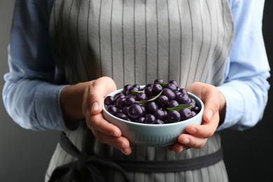 Woman holding tasty acai berries on grey background, closeup