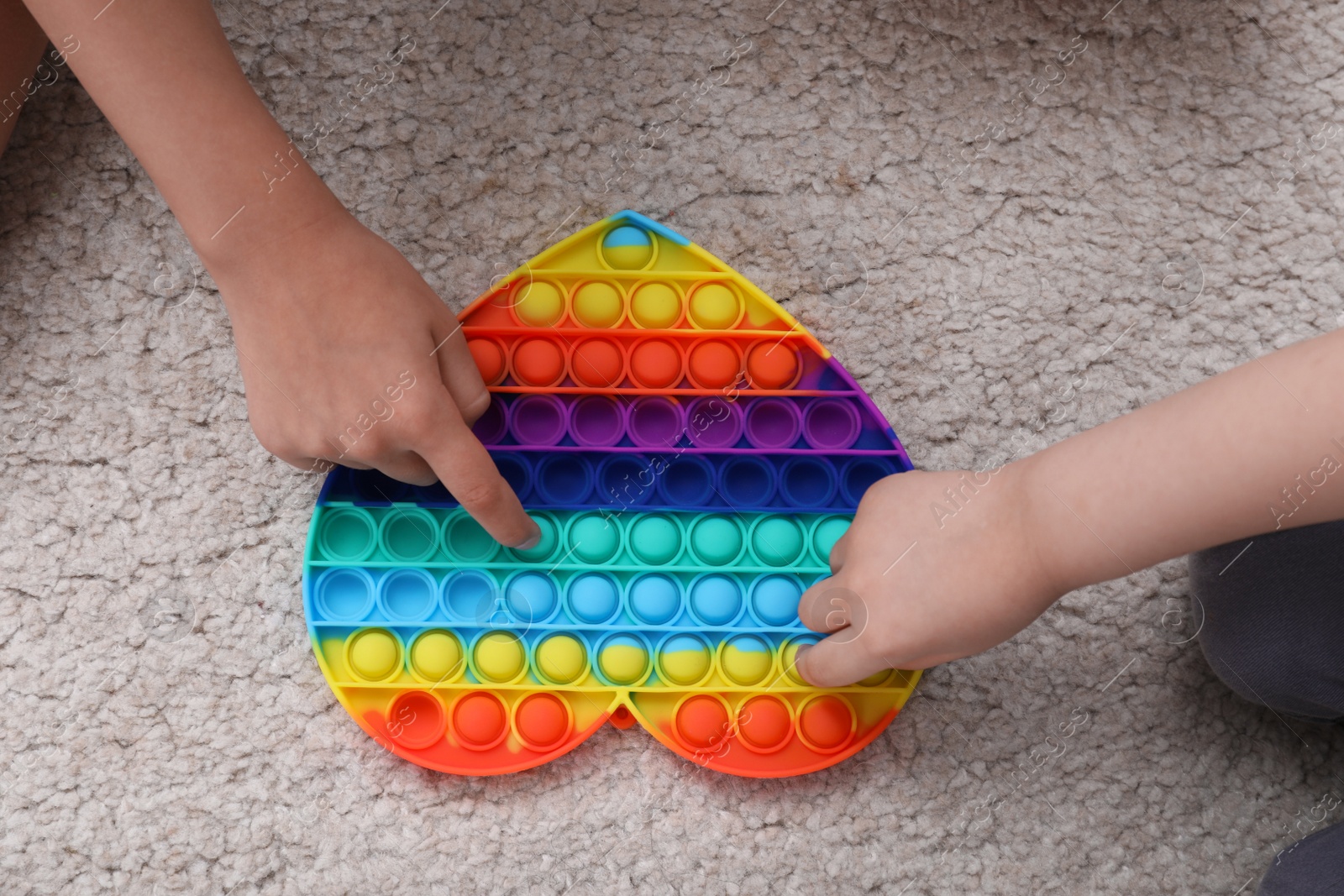 Photo of Little children playing with pop it fidget toy on floor, top view