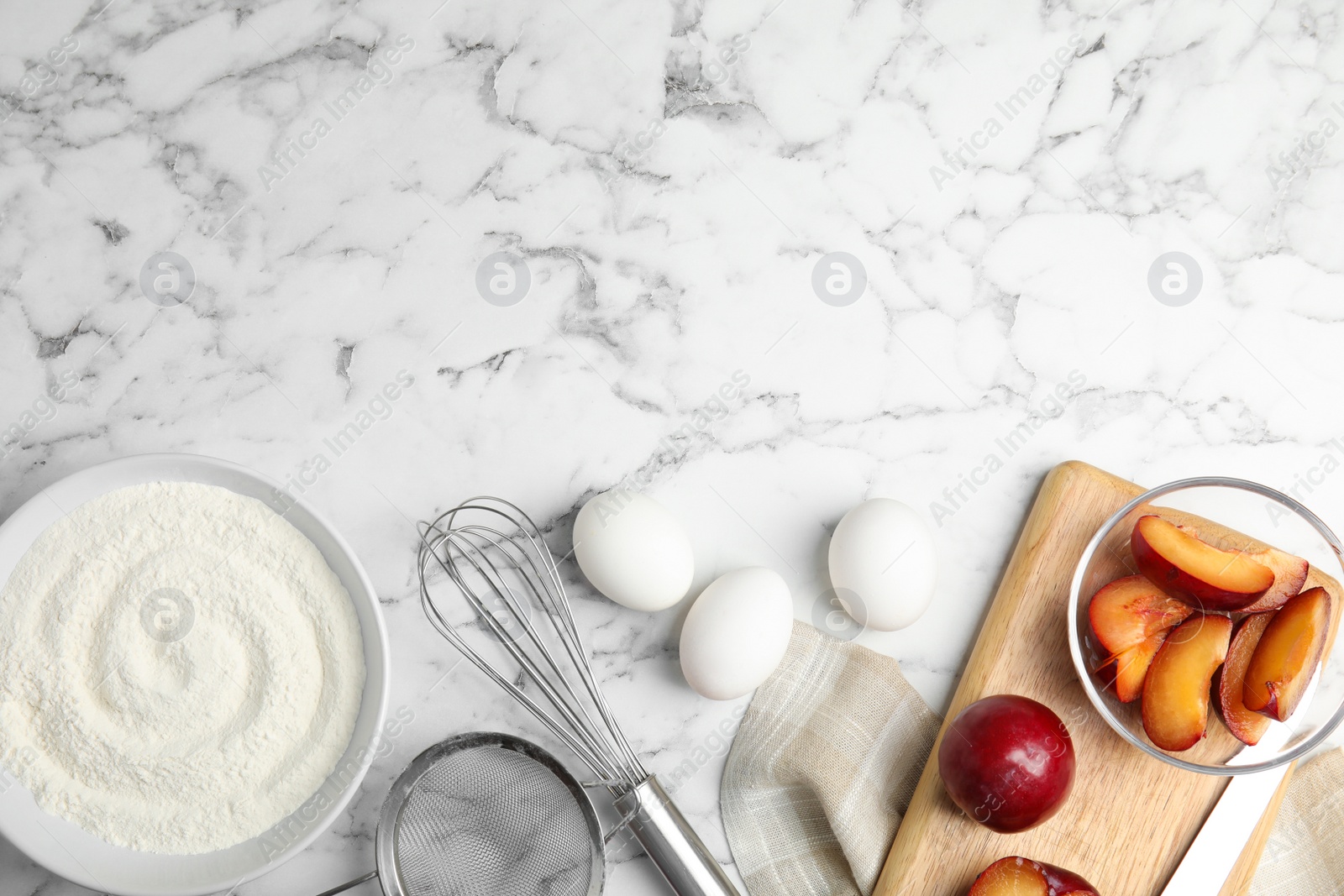 Photo of Fresh eggs and other ingredients on white marble table, flat lay with space for text. Cooking of delicious plum cake