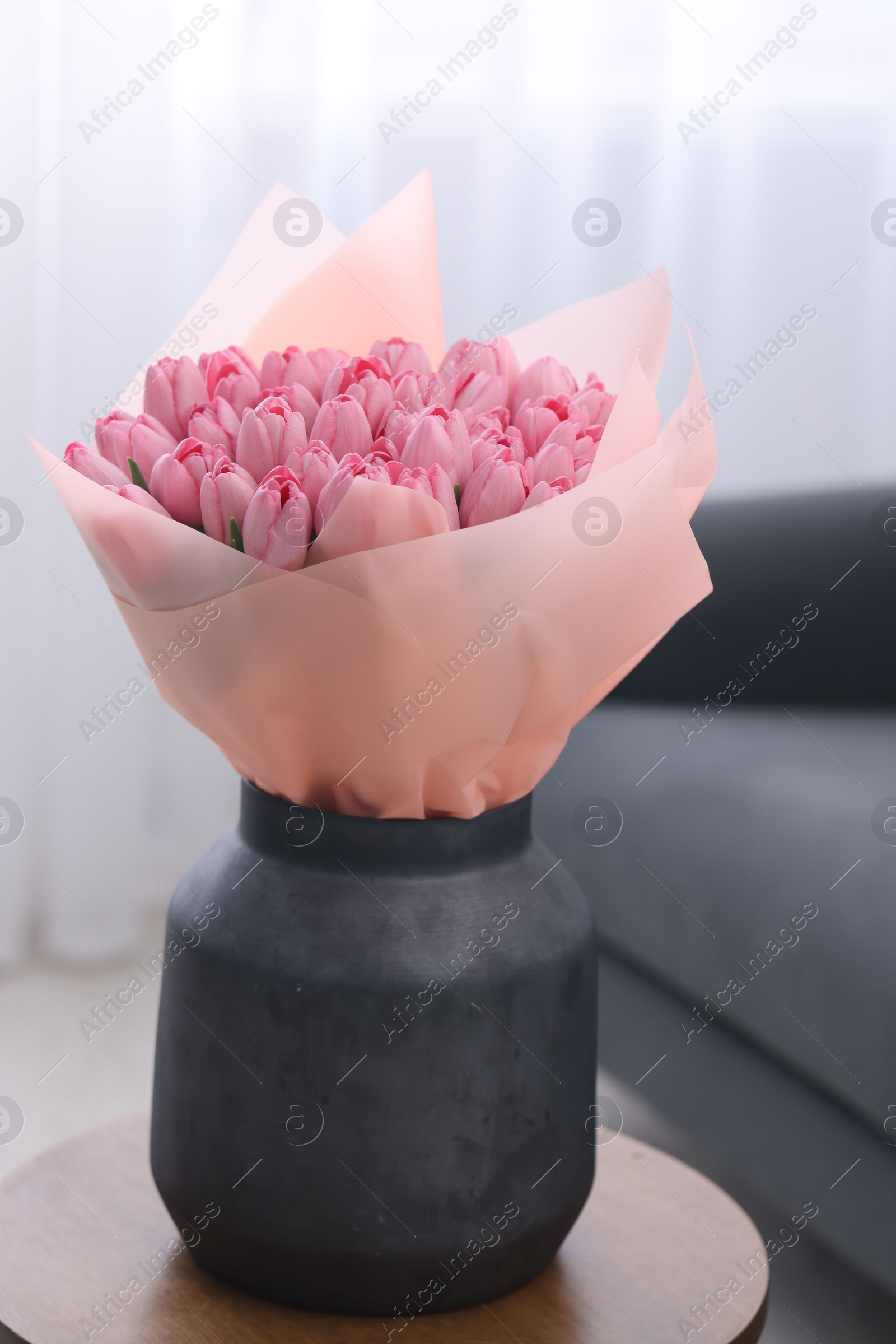 Photo of Bouquet of beautiful pink tulips in vase on wooden table indoors