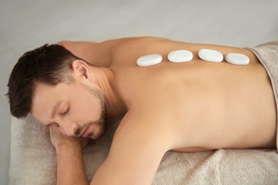 Photo of Handsome man receiving hot stone massage in spa salon