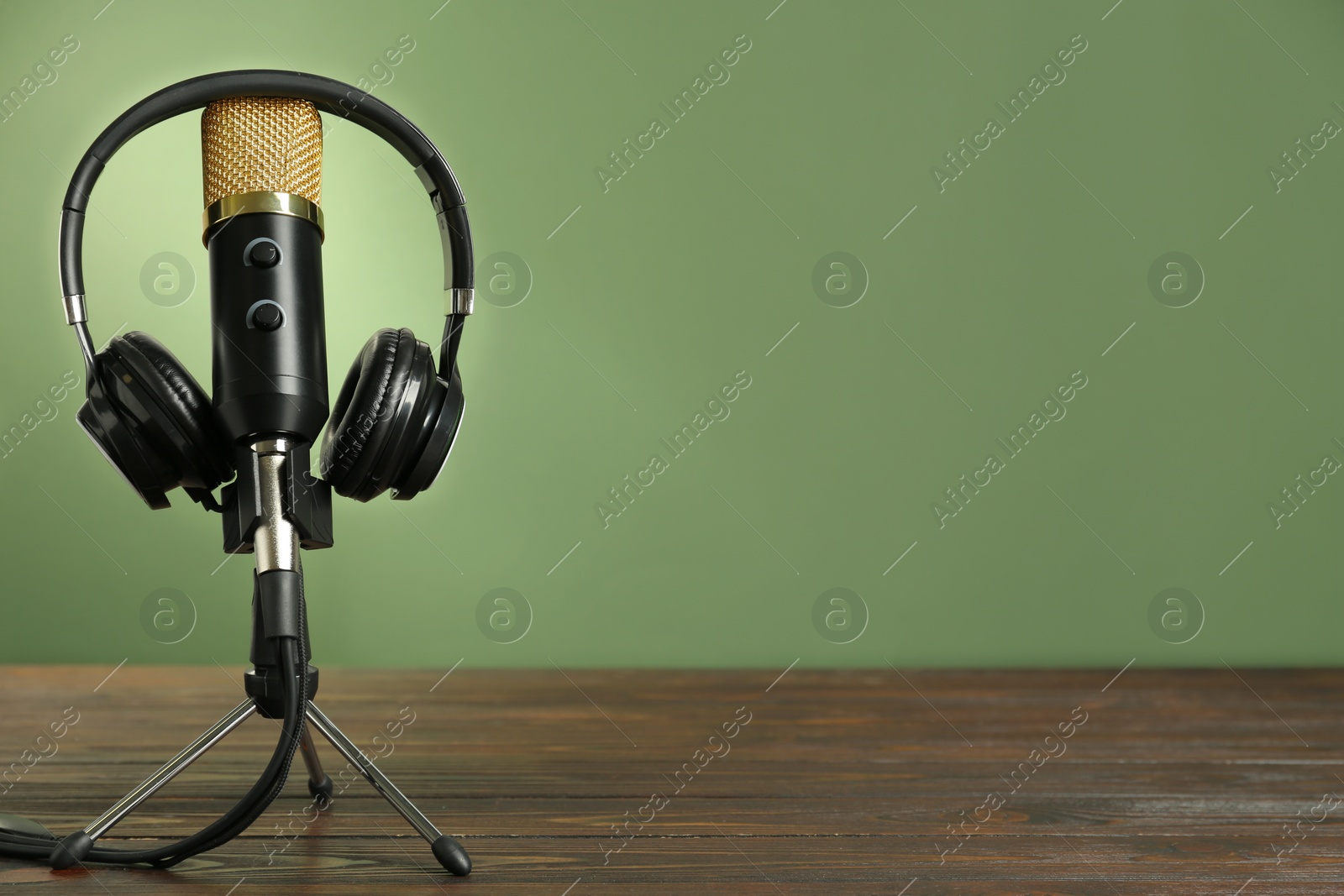 Photo of Microphone and modern headphones on wooden table against green background, space for text