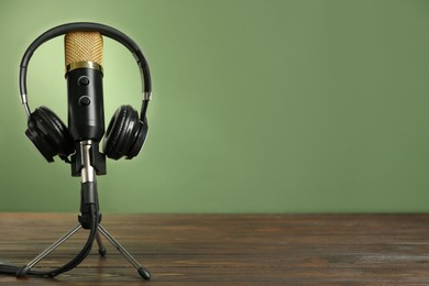 Microphone and modern headphones on wooden table against green background, space for text