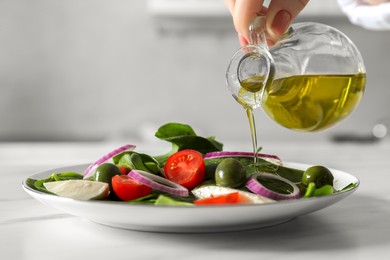 Photo of Woman pouring cooking oil onto plate with salad at white table, closeup