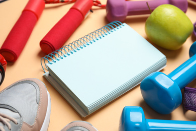 Photo of Composition with fitness equipment, notebook and apple on orange background