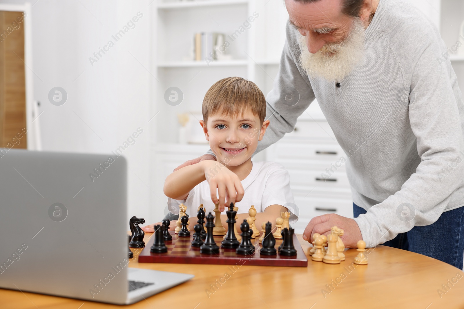 Photo of Grandfather teaching his grandson to play chess following online lesson at home