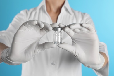 Female doctor holding glass vial on color background, closeup. Medical object