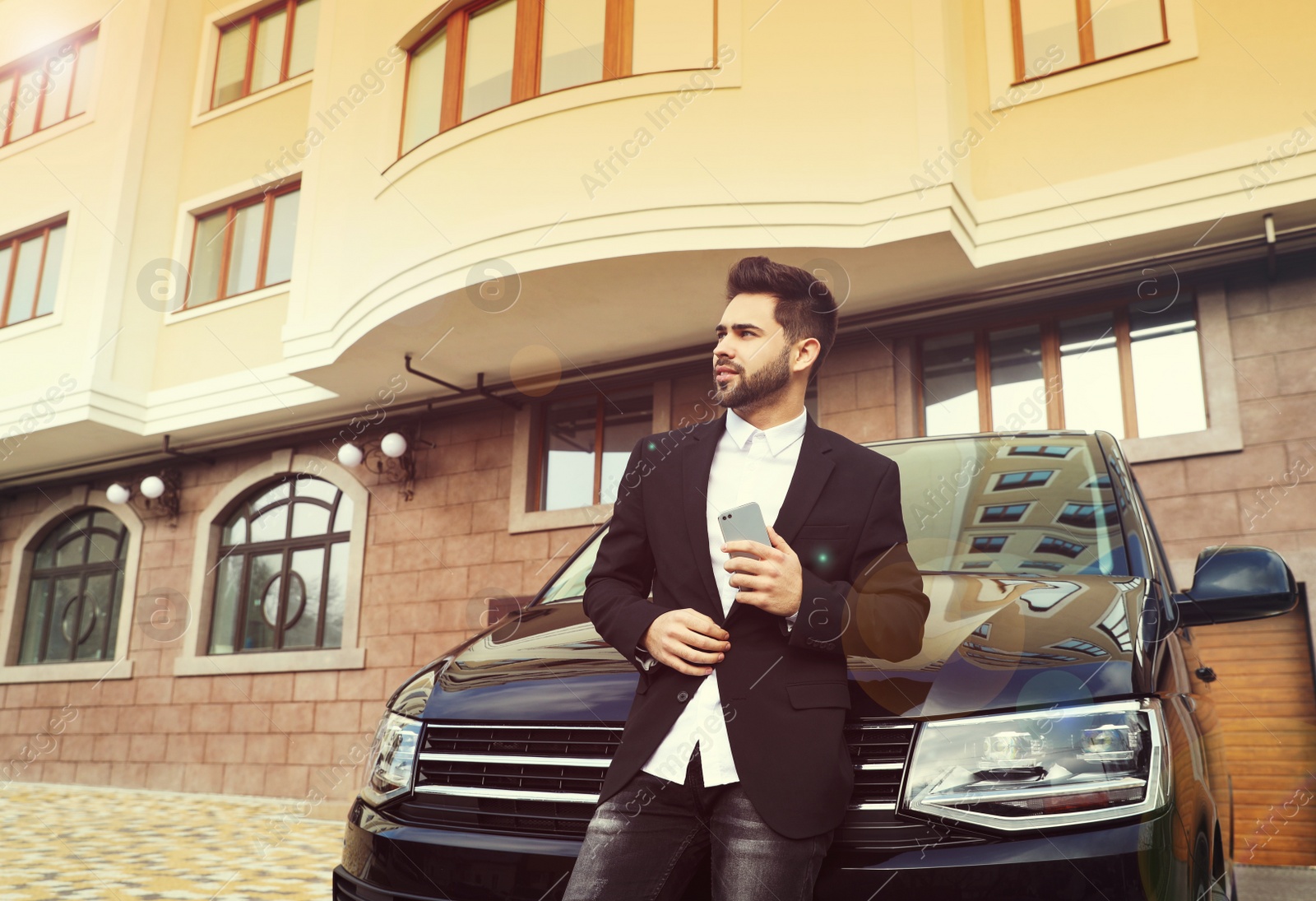 Image of Handsome young man with smartphone near modern car outdoors