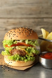 Photo of Burger with delicious patty, french fries and sauce on gray table