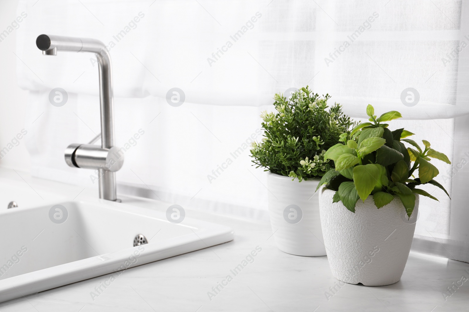 Photo of Artificial potted herbs on white marble countertop near sink in kitchen. Home decor