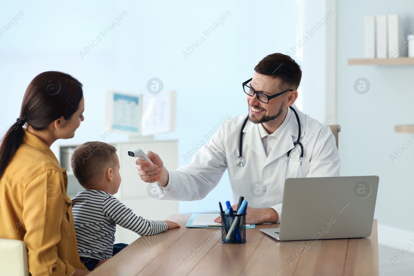 Photo of Mother and son visiting pediatrician in hospital. Doctor checking boy's temperature