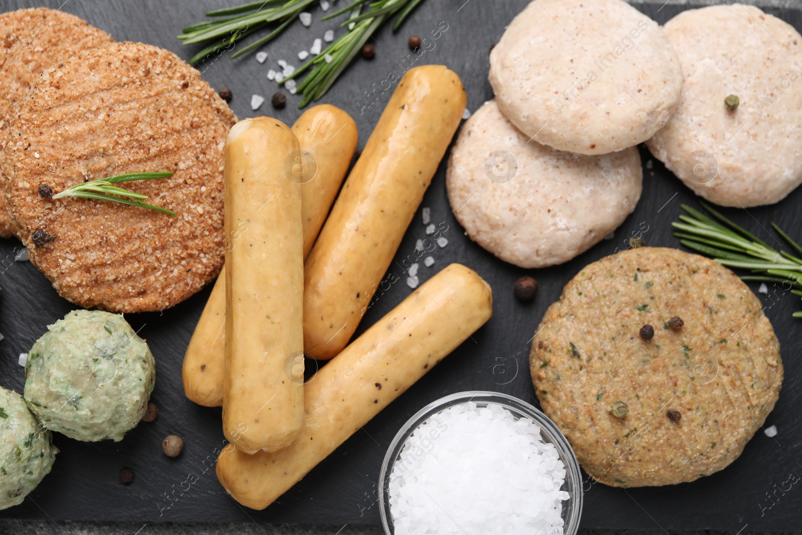 Photo of Different raw vegan meat products, salt and rosemary on dark board, flat lay