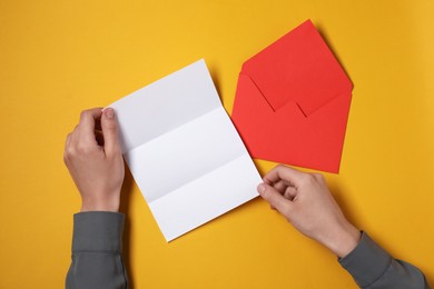 Woman with blank sheet of paper at orange table, top view. Space for text