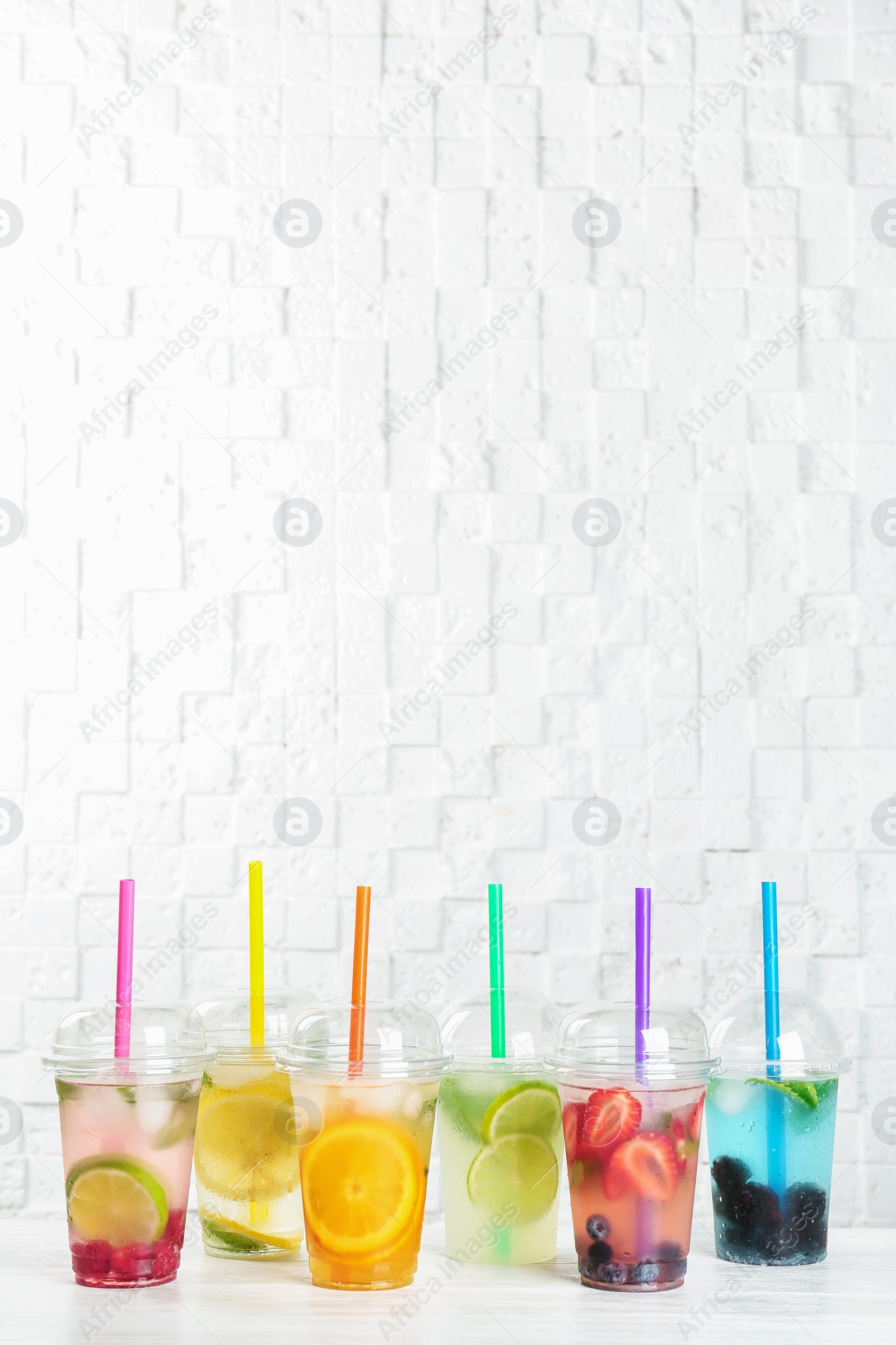 Photo of Plastic cups with lemonades on table near white wall