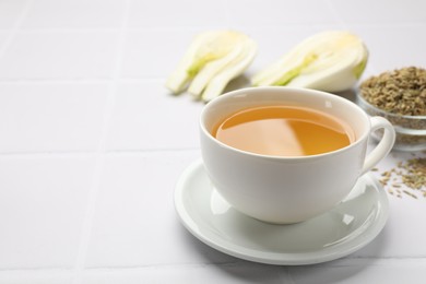 Photo of Fennel tea in cup, seeds and fresh vegetable on white tiled table, closeup. Space for text