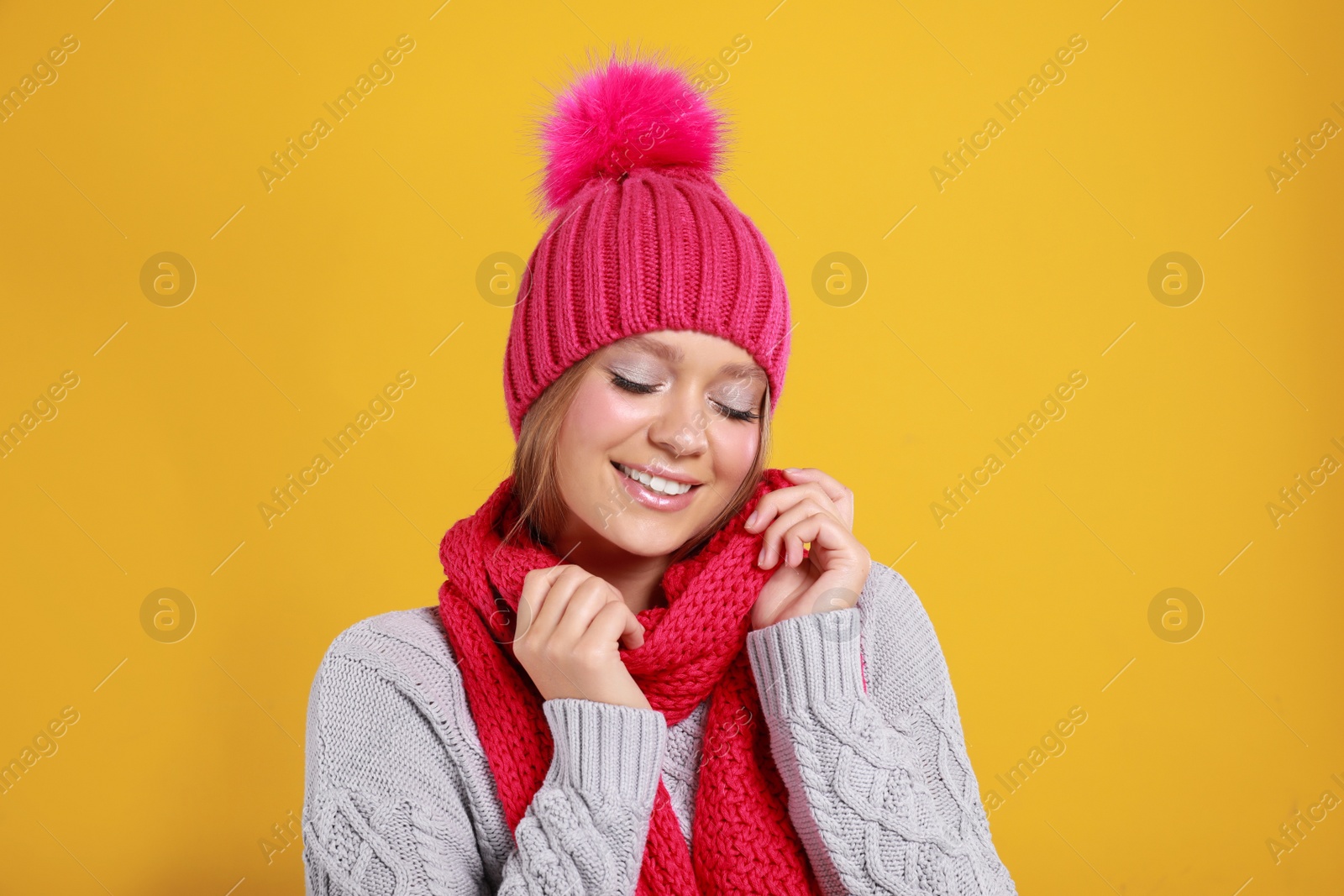 Photo of Young woman in warm sweater, scarf and hat on yellow background. Winter season