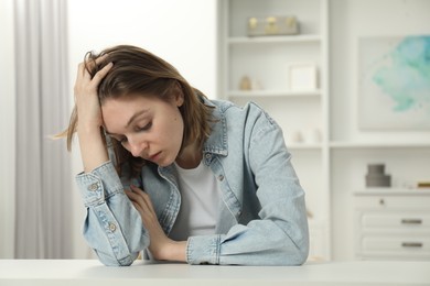 Photo of Sad young woman sitting at white table in room