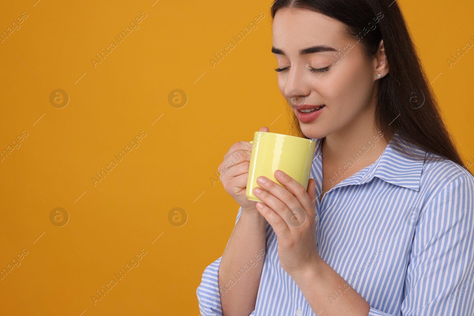 Photo of Beautiful young woman holding yellow ceramic mug on orange background, space for text