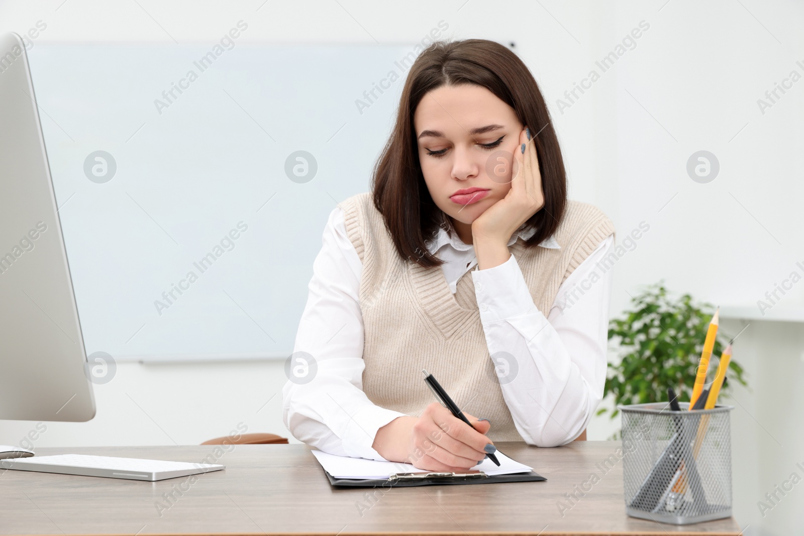 Photo of Puzzled young intern writing at table in modern office. First work day