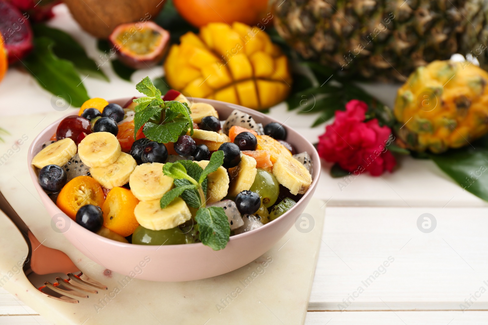 Photo of Delicious exotic fruit salad served on white table. Space for text