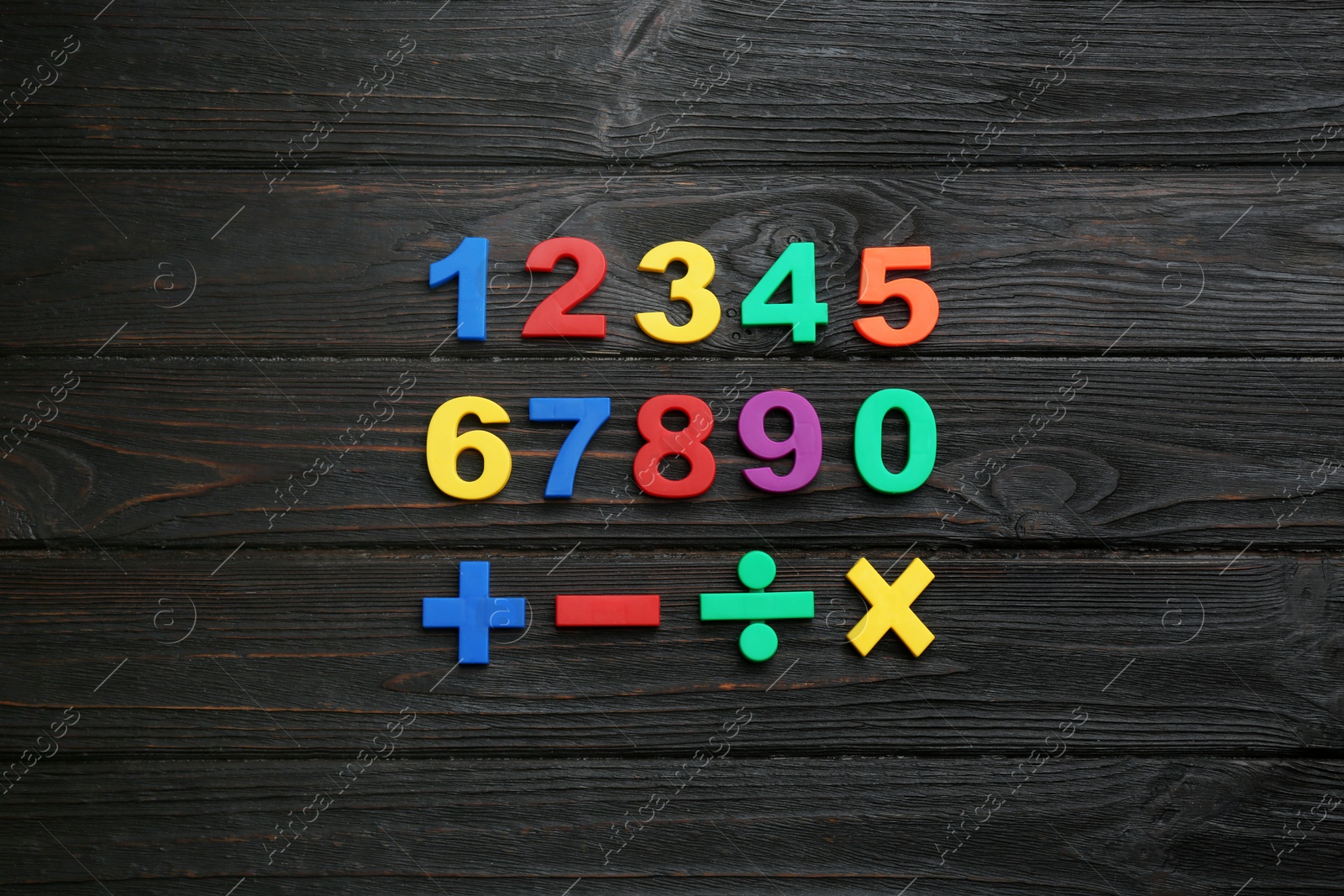 Photo of Colorful magnetic numbers and math symbols on black wooden background, flat lay