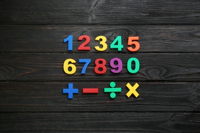 Photo of Colorful magnetic numbers and math symbols on black wooden background, flat lay