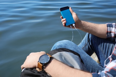 Photo of Man charging mobile phone with power bank near river, closeup