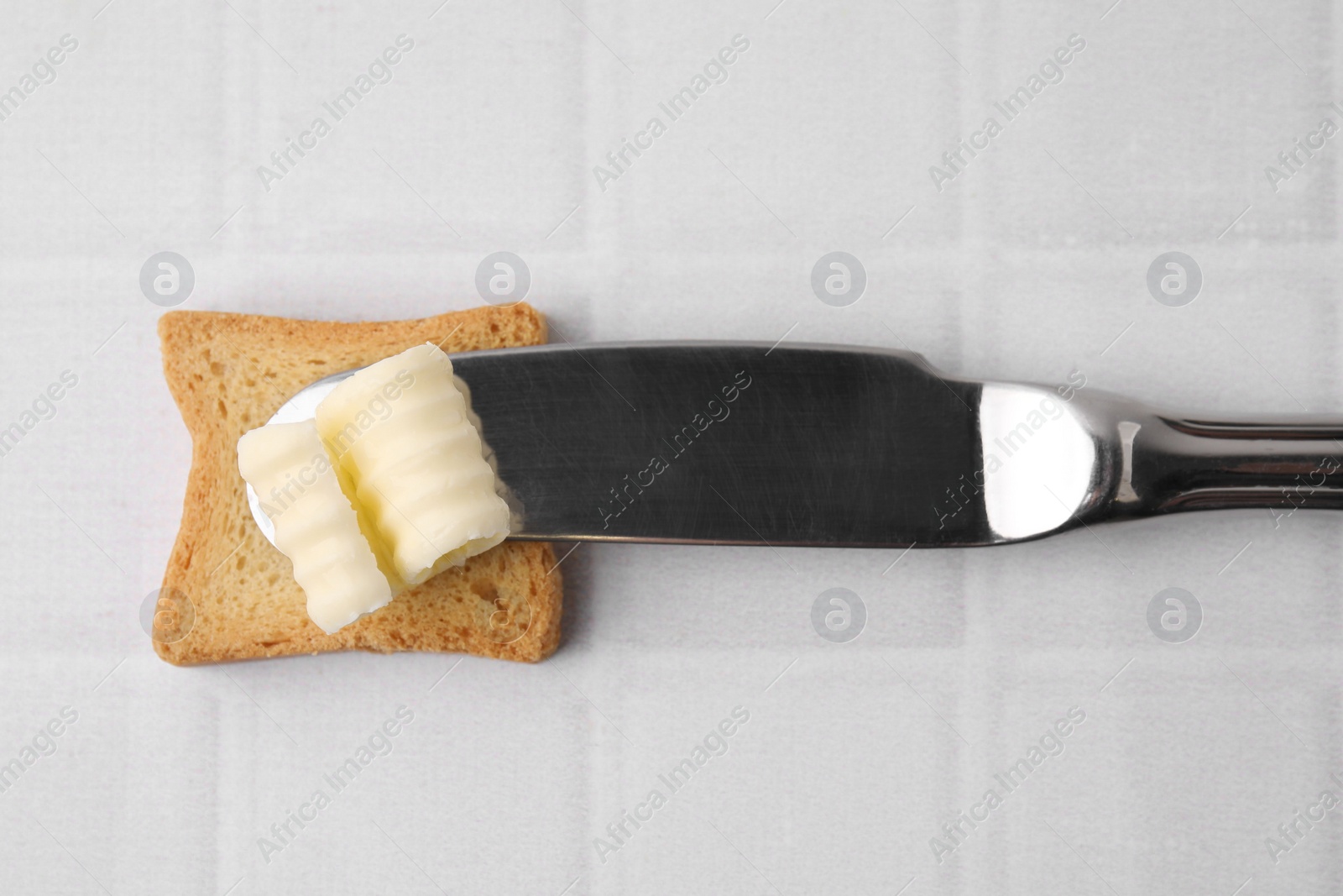 Photo of Tasty butter curl, knife and piece of dry bread on white tiled table, top view