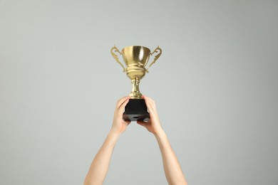 Photo of Man holding gold trophy cup on light grey background, closeup