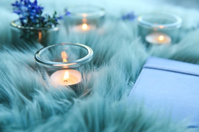 Photo of Burning candles in glass holders and notebook on fur fabric