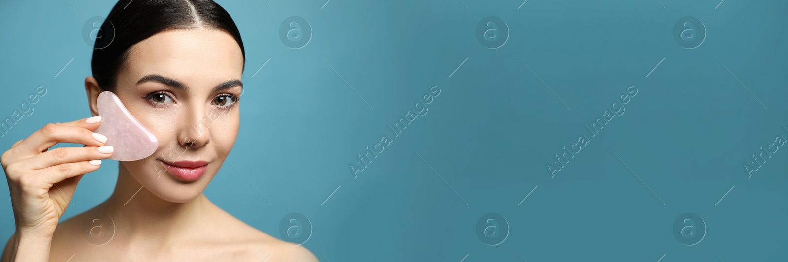 Image of Beautiful young woman doing facial massage with gua sha tool on blue background, space for text. Banner design