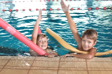 Little boys with swimming noodles in indoor pool