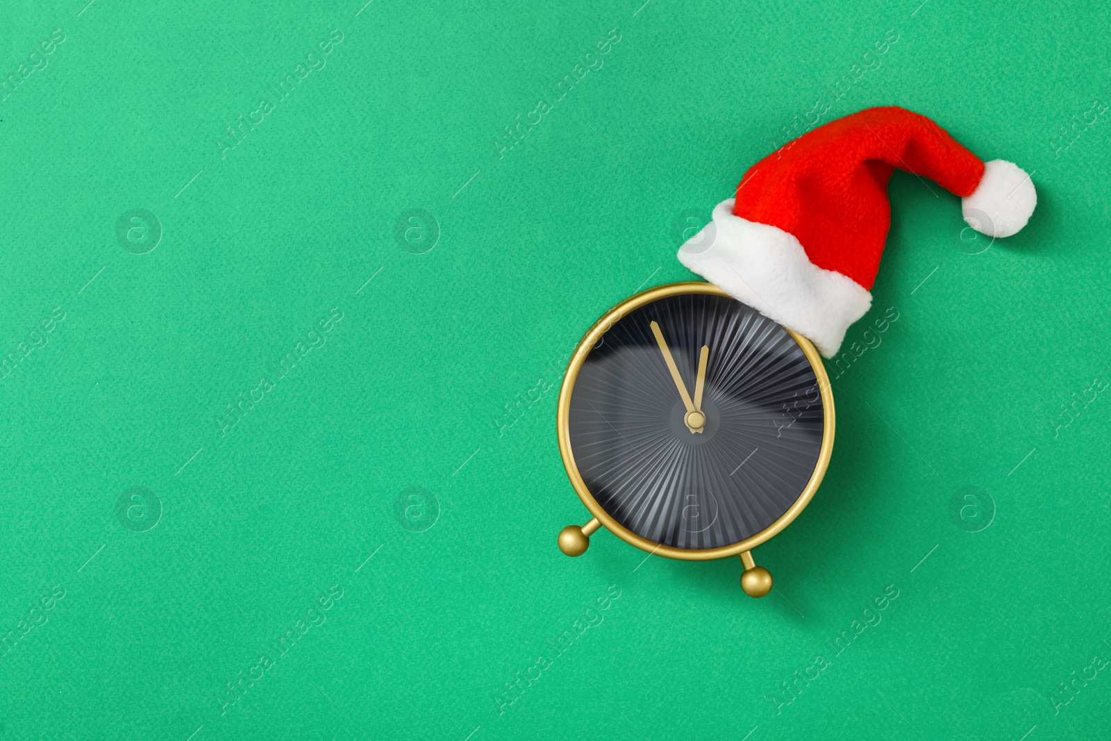 Photo of Alarm clock in Santa hat on green background, top view with space for text. New Year countdown
