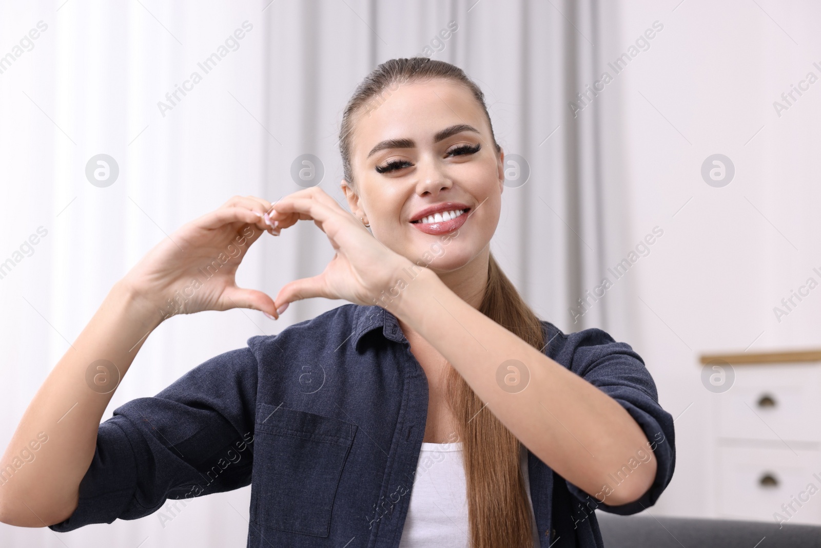 Photo of Happy woman showing heart gesture with hands at home