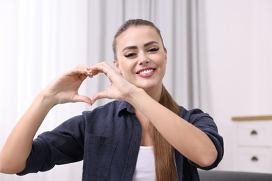 Happy woman showing heart gesture with hands at home