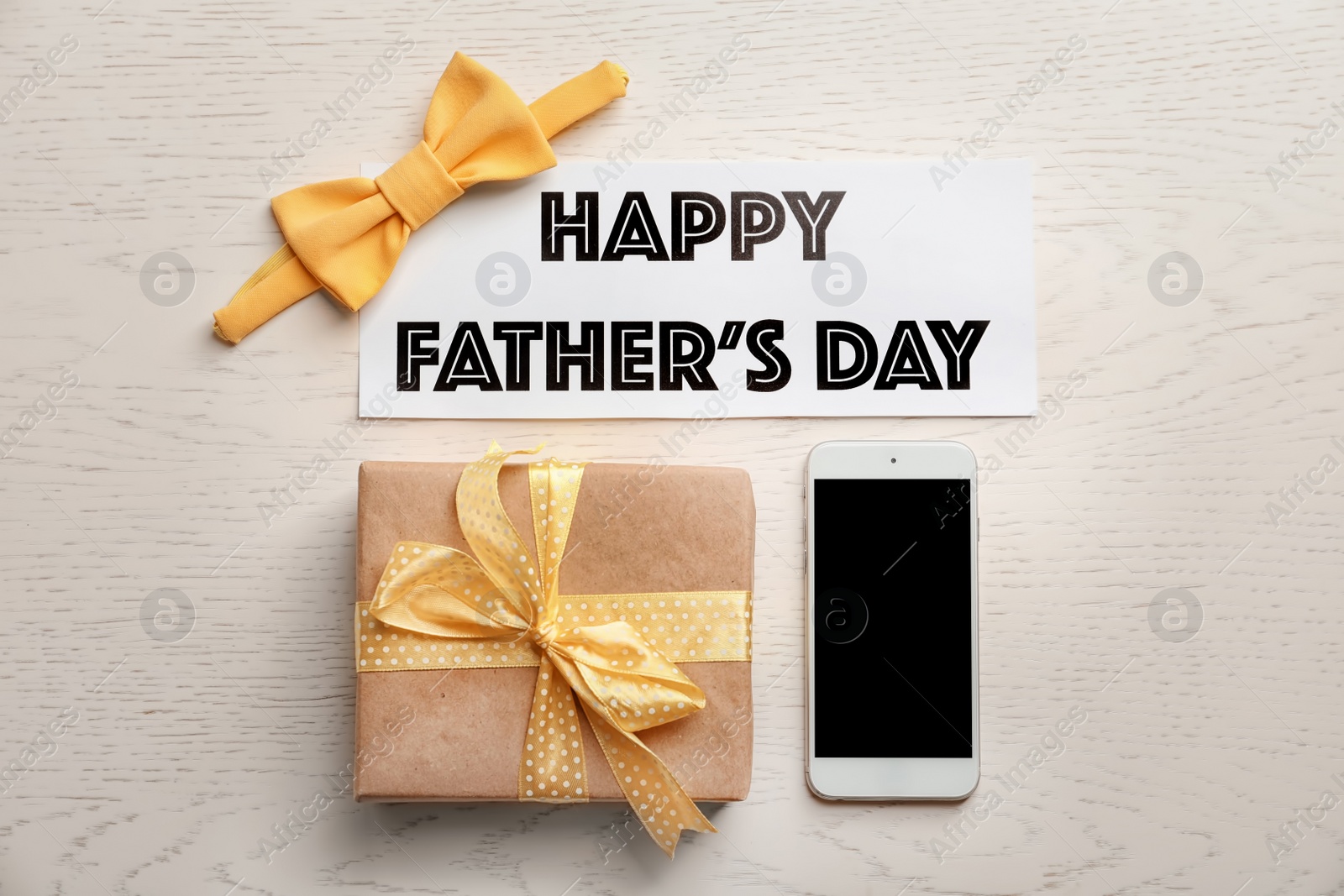 Photo of Gift box, bow tie, smartphone and card with words HAPPY FATHER'S DAY on light background, top view