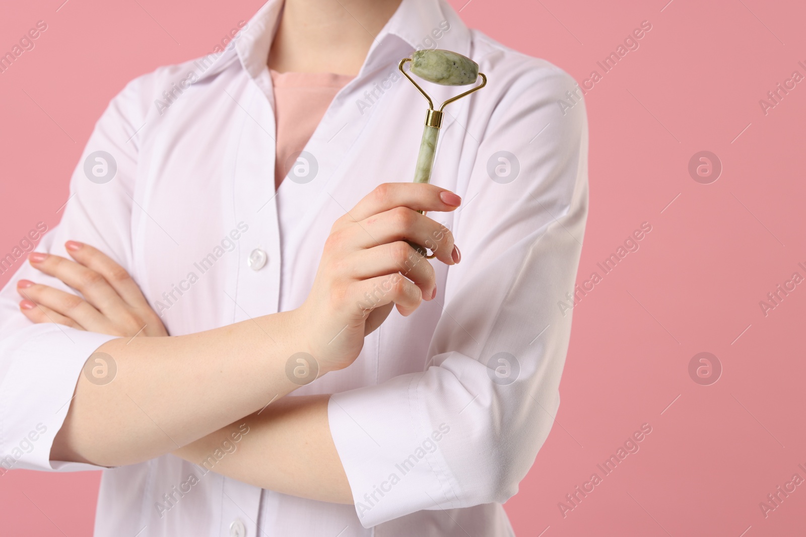 Photo of Cosmetologist with facial roller on pink background, closeup