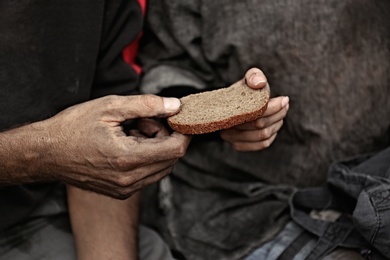 Photo of Poor homeless people sharing piece of bread outdoors, closeup