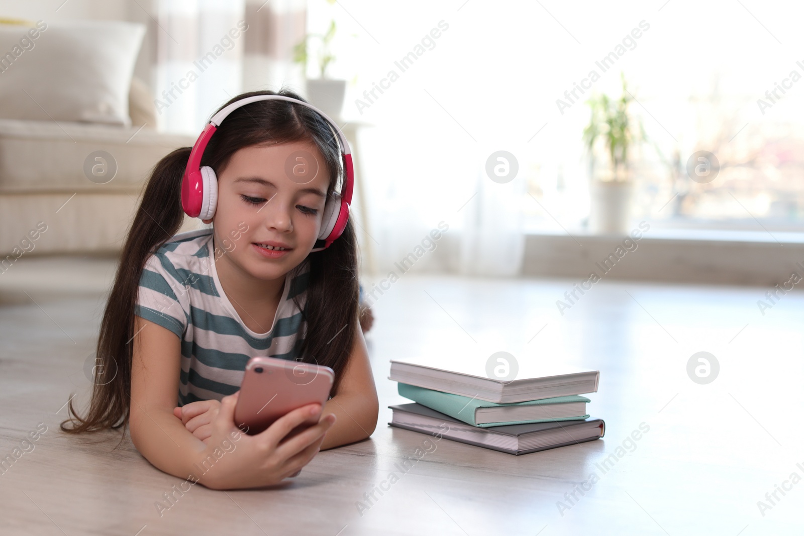 Photo of Cute little girl with headphones and smartphone listening to audiobook at home