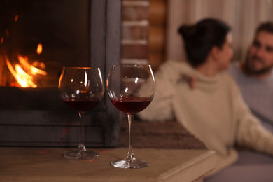 Photo of Lovely couple near fireplace at home, focus on glasses with wine. Winter vacation