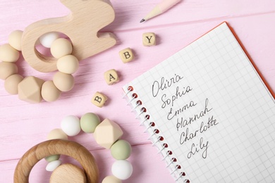 Photo of List of baby names and child's toys on pink wooden background, flat lay