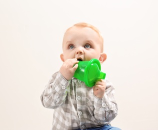Photo of Little boy with sippy cup on light background. Baby accessories