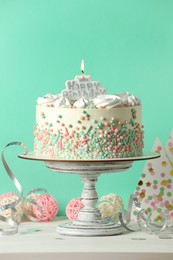 Photo of Delicious birthday cake and party decor on white wooden table against turquoise background
