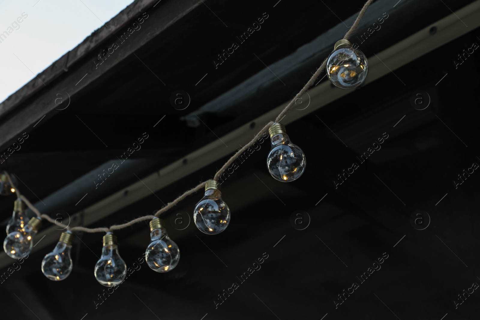 Photo of Beautiful garland of lamp bulbs hanging outdoors. String lights