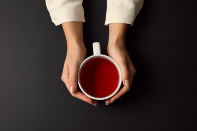 Woman with cup of tea on black background, top view