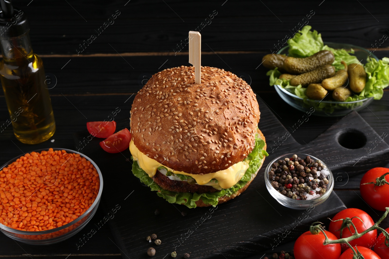 Photo of Tasty vegetarian burger and ingredients on black wooden table