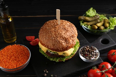 Tasty vegetarian burger and ingredients on black wooden table