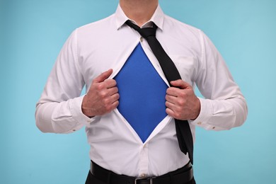 Photo of Businessman wearing superhero costume under suit on light blue background, closeup