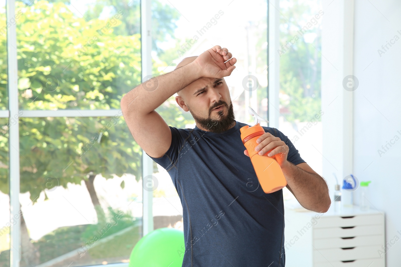 Photo of Tired overweight man with bottle of water in gym